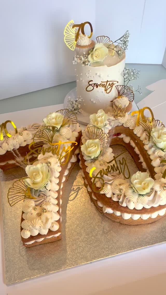 White and gold 70th birthday cakes decorated with cream roses and gold toppers.