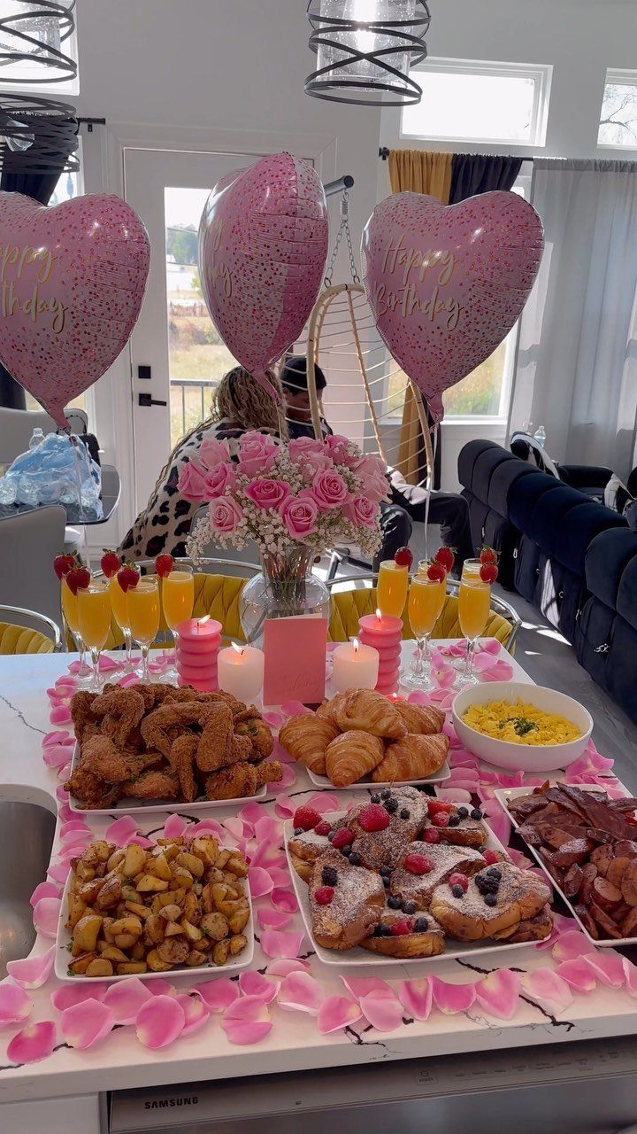 Celebratory breakfast spread with pink heart balloons, roses, and pastries on a counter.
