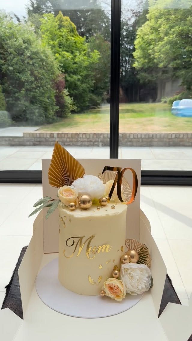 Cream birthday cake with gold Mum and 70 toppers, roses, and gold spheres.