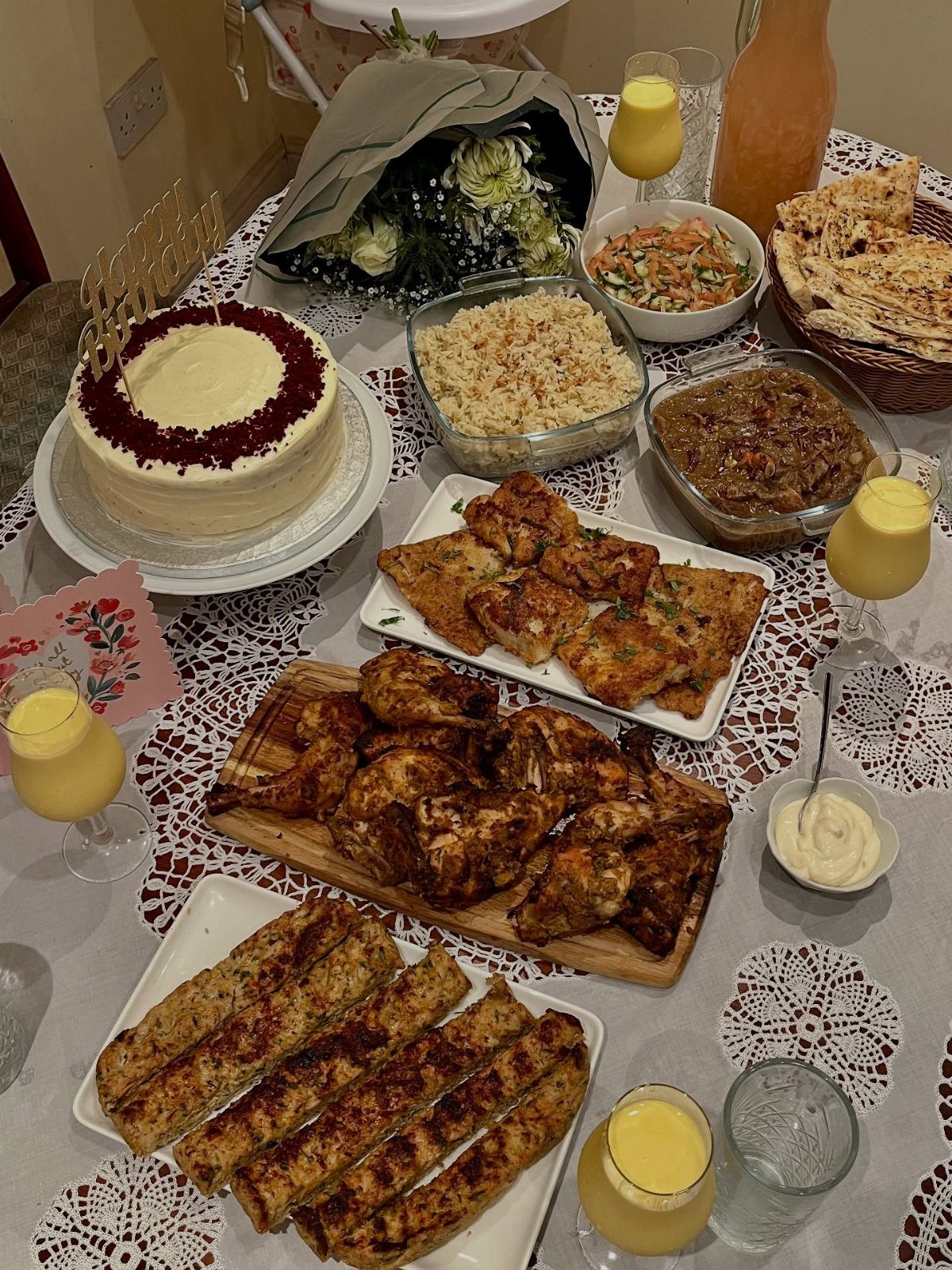 Festive birthday meal spread with cake, roasted chicken, and various side dishes on lace.
