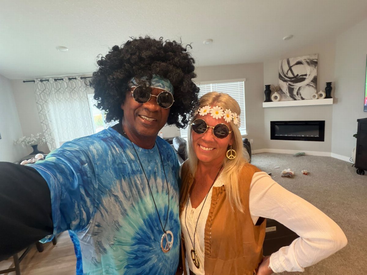 Man and woman in 1960s hippie costumes posing for a selfie indoors.