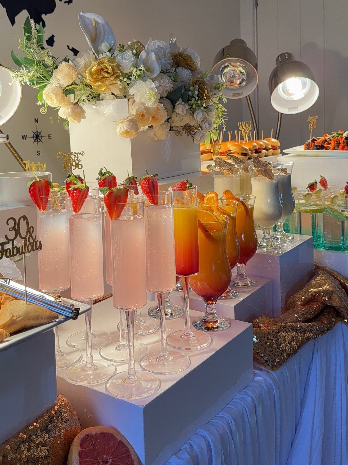 Celebratory cocktail and appetizer spread with a 30th birthday sign and white flowers.