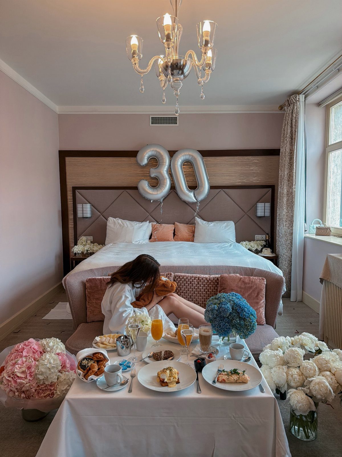 Woman in a white robe enjoying breakfast in a hotel room with 30th birthday balloons.