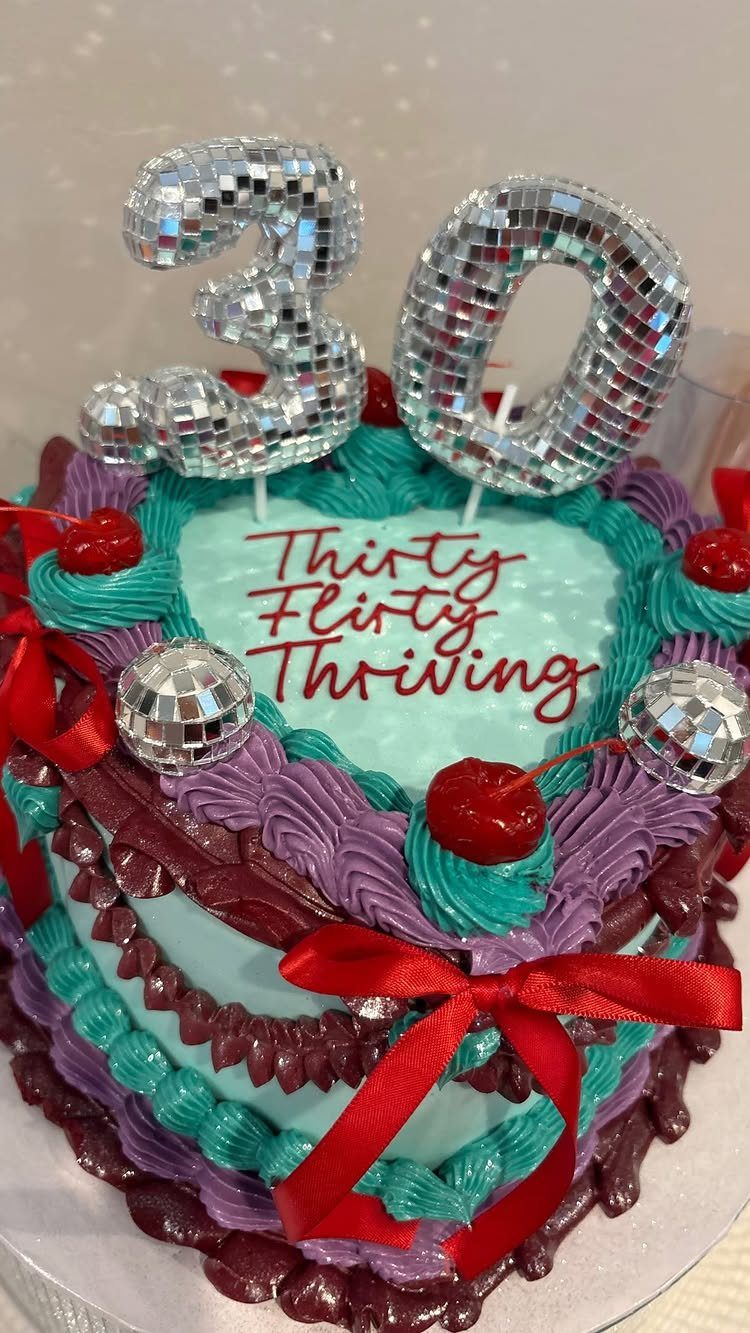 Heart-shaped 30th birthday cake with colorful frosting, disco balls, and red ribbons.