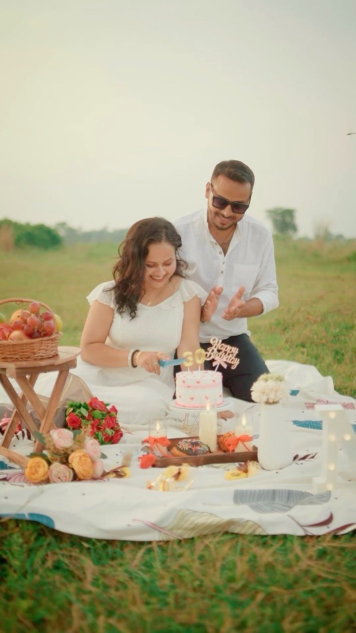 Couple celebrating a birthday with a cake and picnic setup in a field
