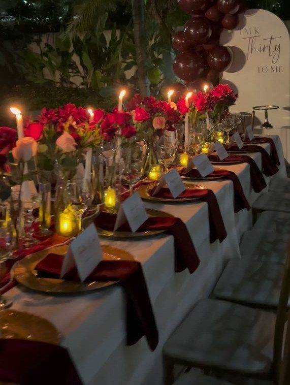 Elegant party table with red roses, gold plates, and a 30th birthday sign.