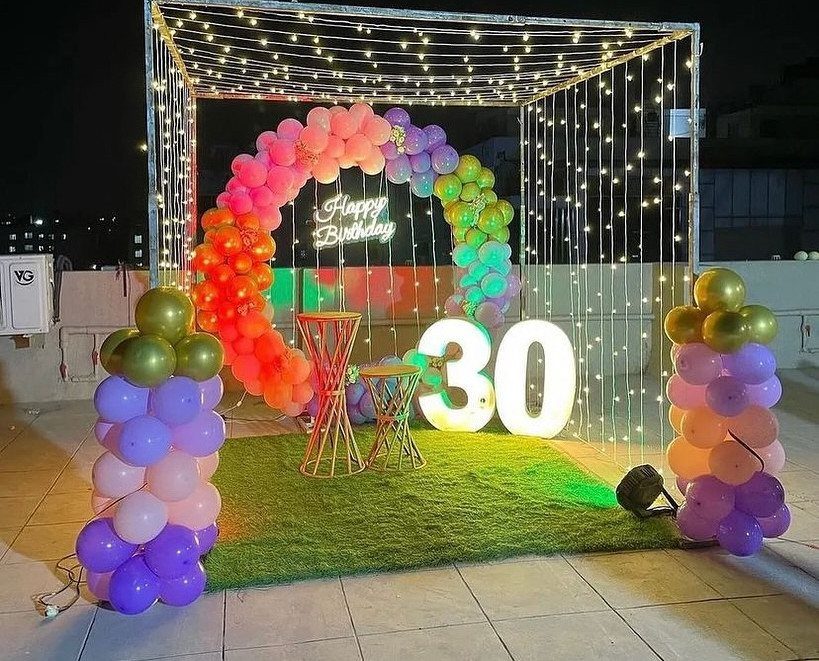 Colorful balloon arch and glowing number 30 on a lit rooftop terrace