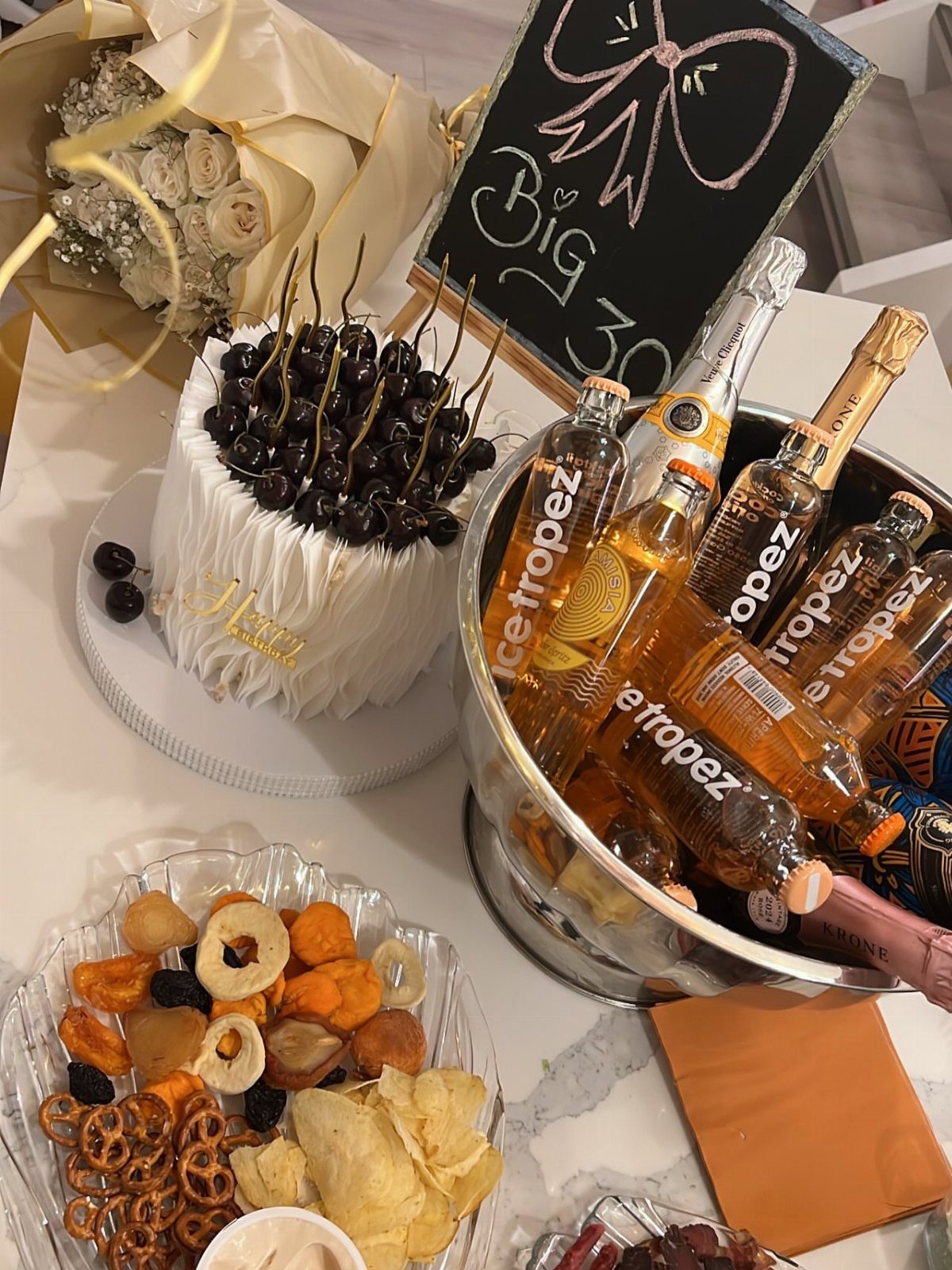 Birthday celebration setup with a cherry cake, champagne bucket, and Big 30 sign.