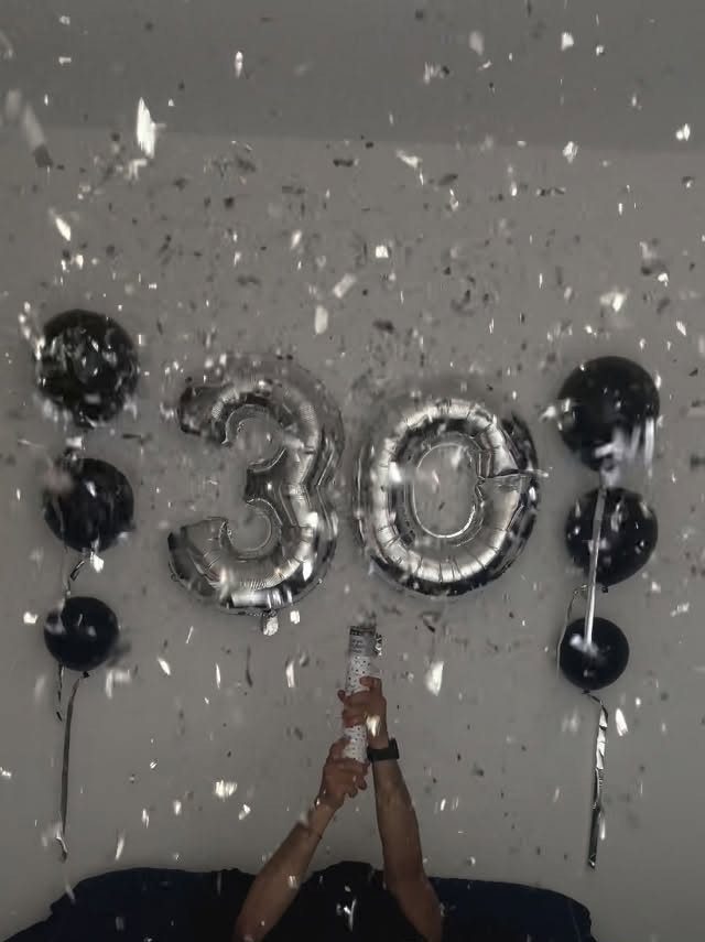 Silver number 30 balloons and black balloons with falling silver confetti.