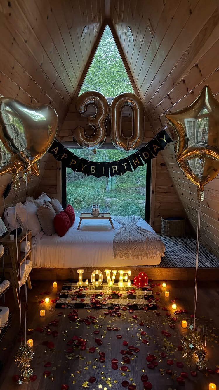 Bedroom in a wooden cabin decorated with gold 30 balloons and rose petals.