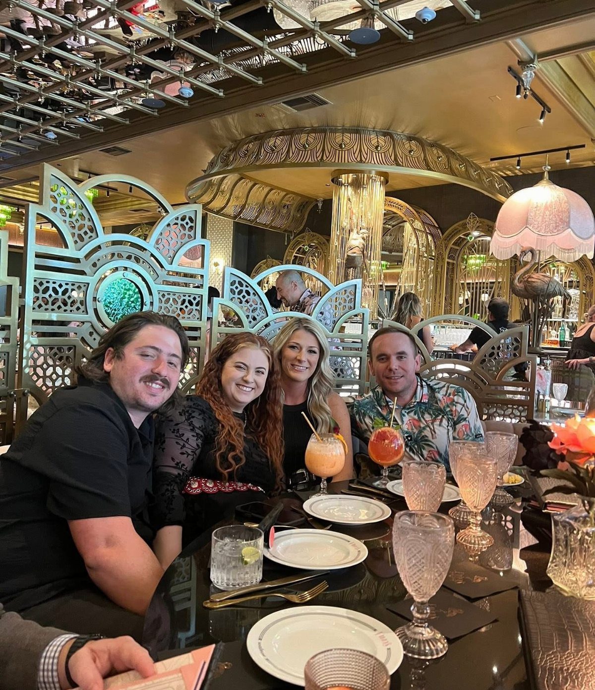 Four smiling adults dining at a fancy restaurant with gold decor and drinks.