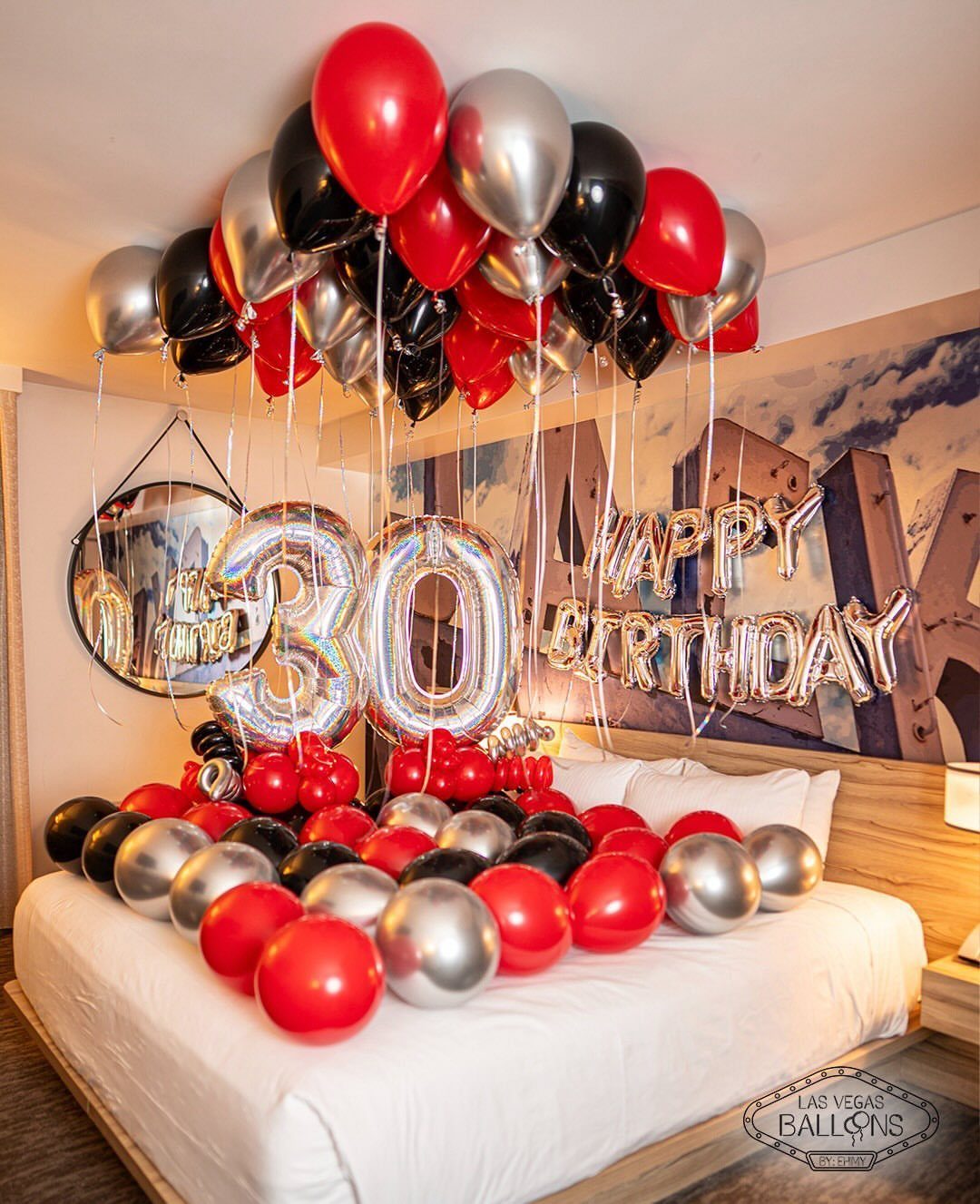 Hotel bed decorated with red, black, and silver balloons for a 30th birthday.