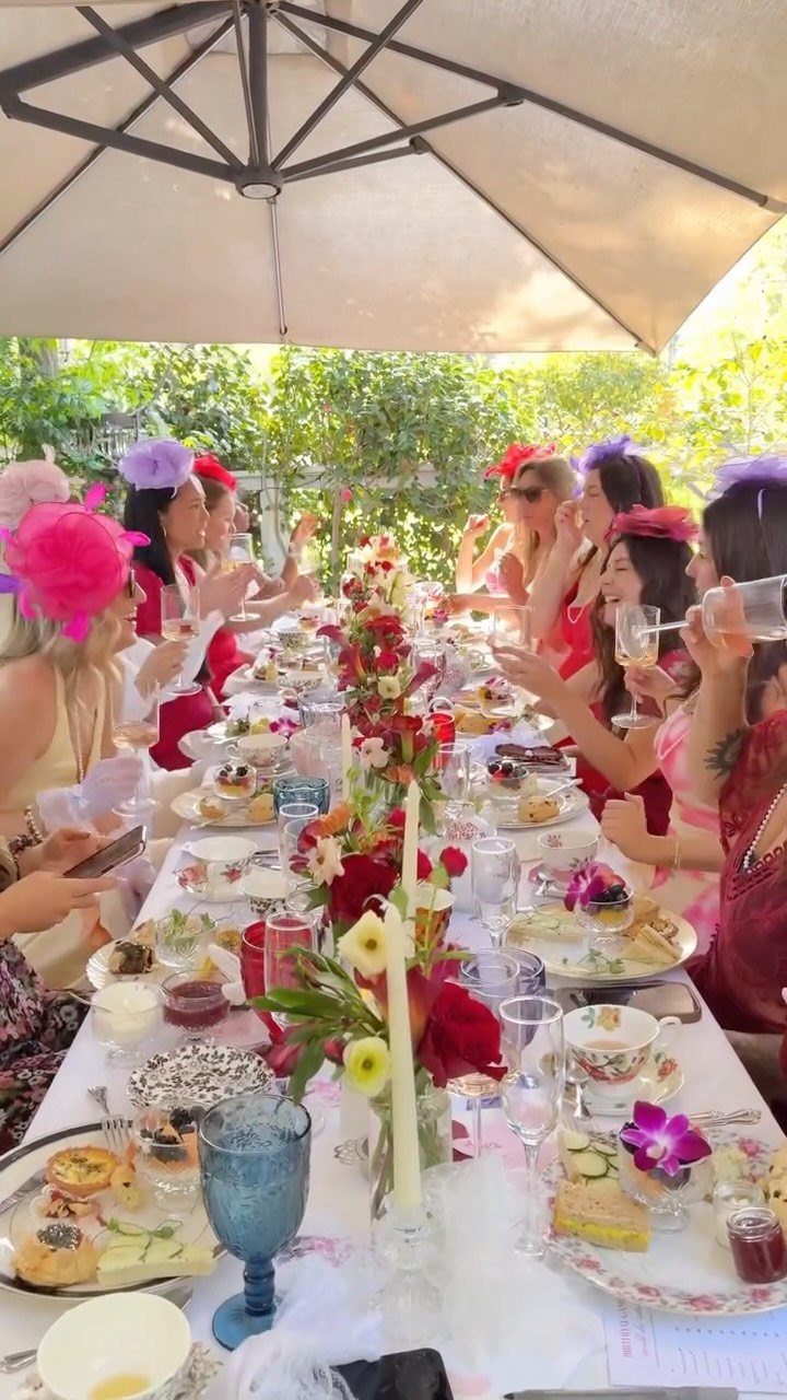 Women in fascinators enjoying tea and finger sandwiches at an outdoor garden party.