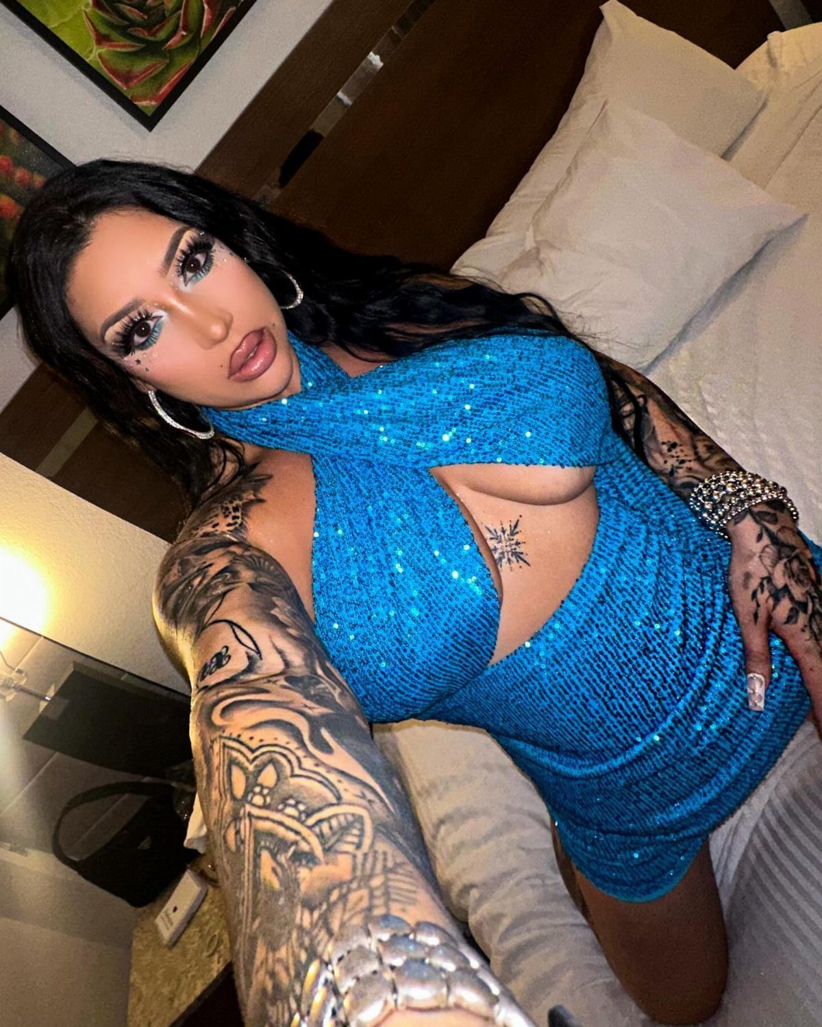 Woman in a sparkling blue sequined dress posing for a selfie in a hotel.