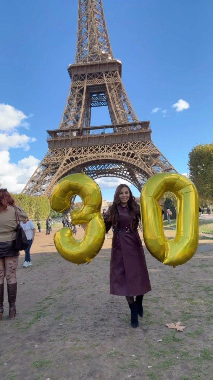 Woman in purple dress holding gold 30 balloons in front of Eiffel Tower