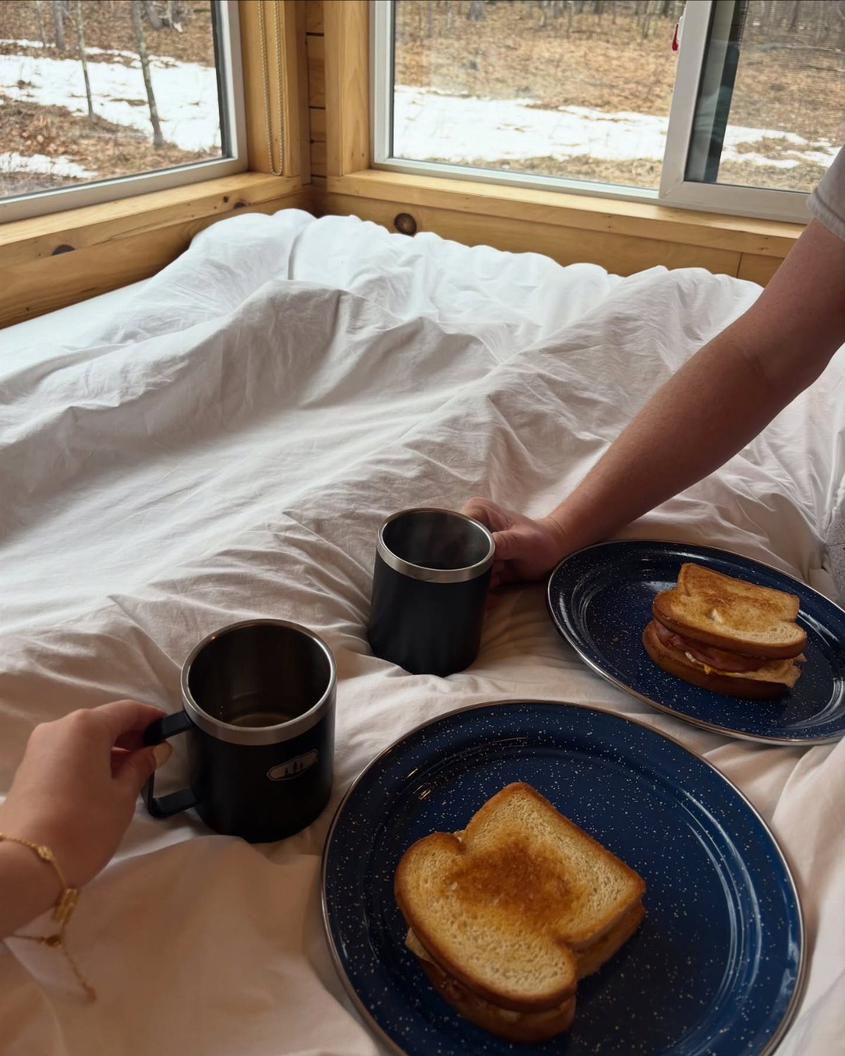 Breakfast in bed with toasted sandwiches and coffee overlooking a snowy winter landscape