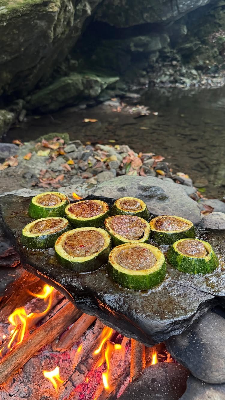Stuffed zucchini rounds grilling on a hot stone over an outdoor campfire.