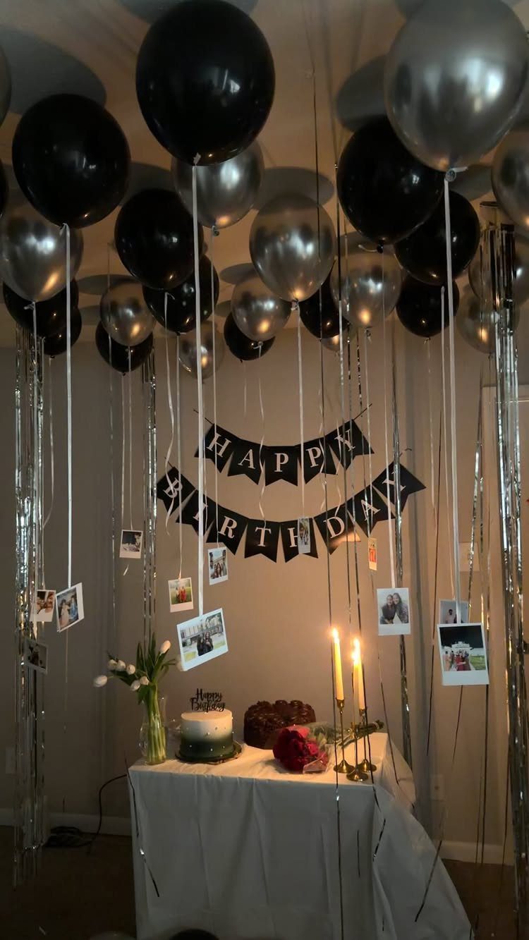 Birthday party decorations with black and silver balloons, banner, and cake on table.