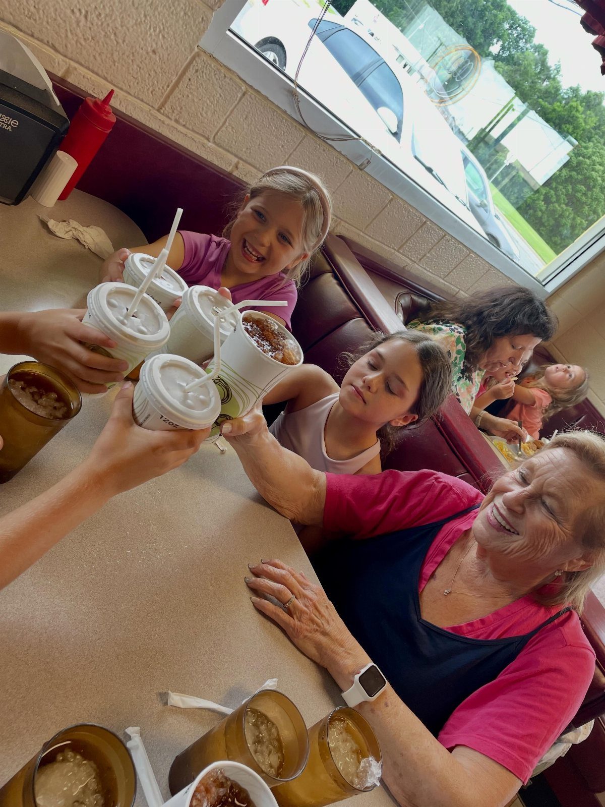 Women and girls clinking coffee cups together while sitting in a diner booth.