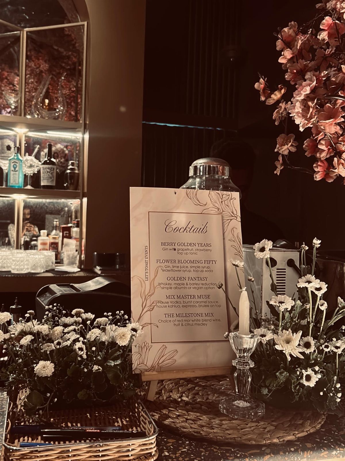 Cocktail menu on an easel surrounded by white flowers and a candle at a bar