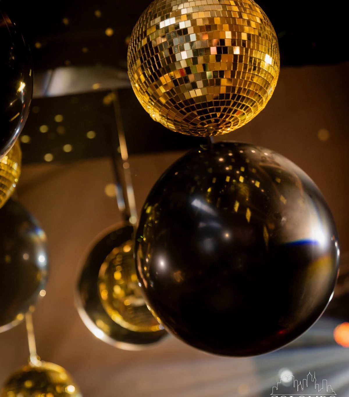 Gold disco ball and black balloons decorating a dark party venue.