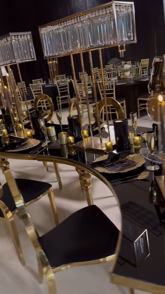 Elegant black and gold banquet table setting with crystal candle holders and chairs.