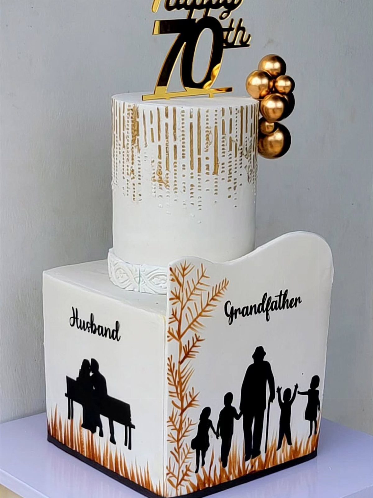 Two-tiered white birthday cake with gold 70 topper and family silhouettes.