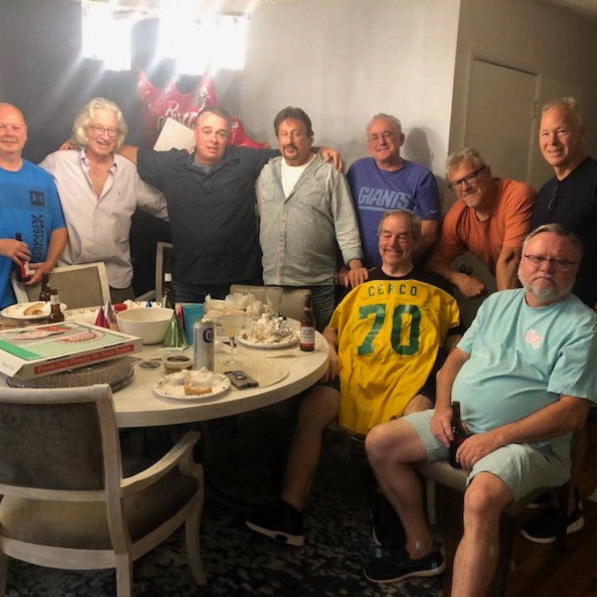 Group of older men celebrating a 70th birthday around a dining table.