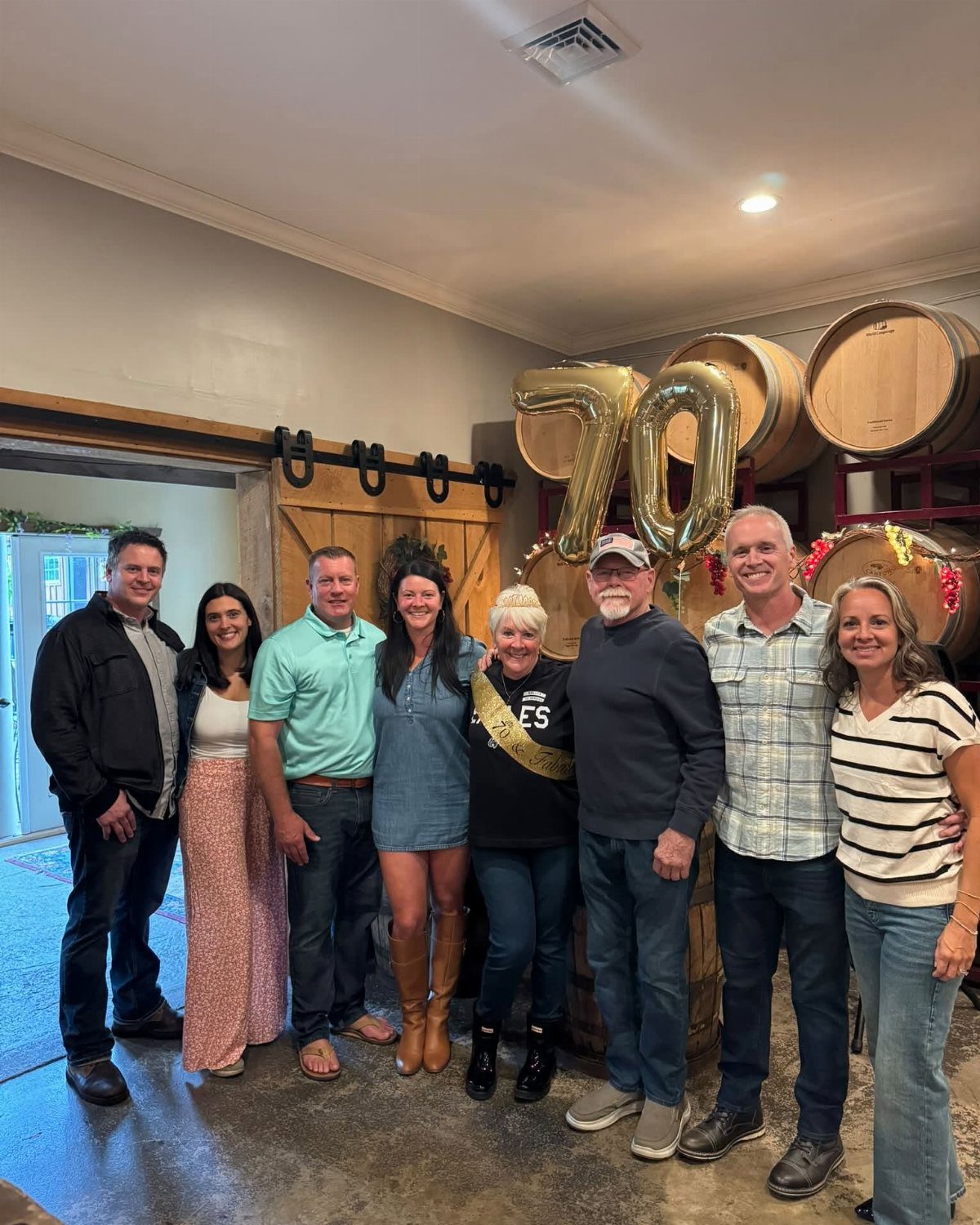 Group of family members posing together in front of gold 70 balloons and barrels.