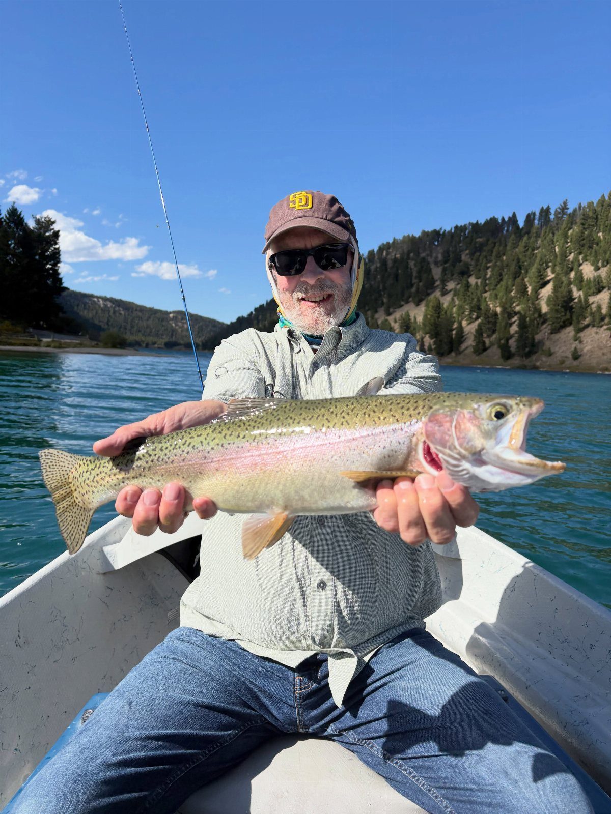 Older man in a boat holding a large rainbow trout on a lake