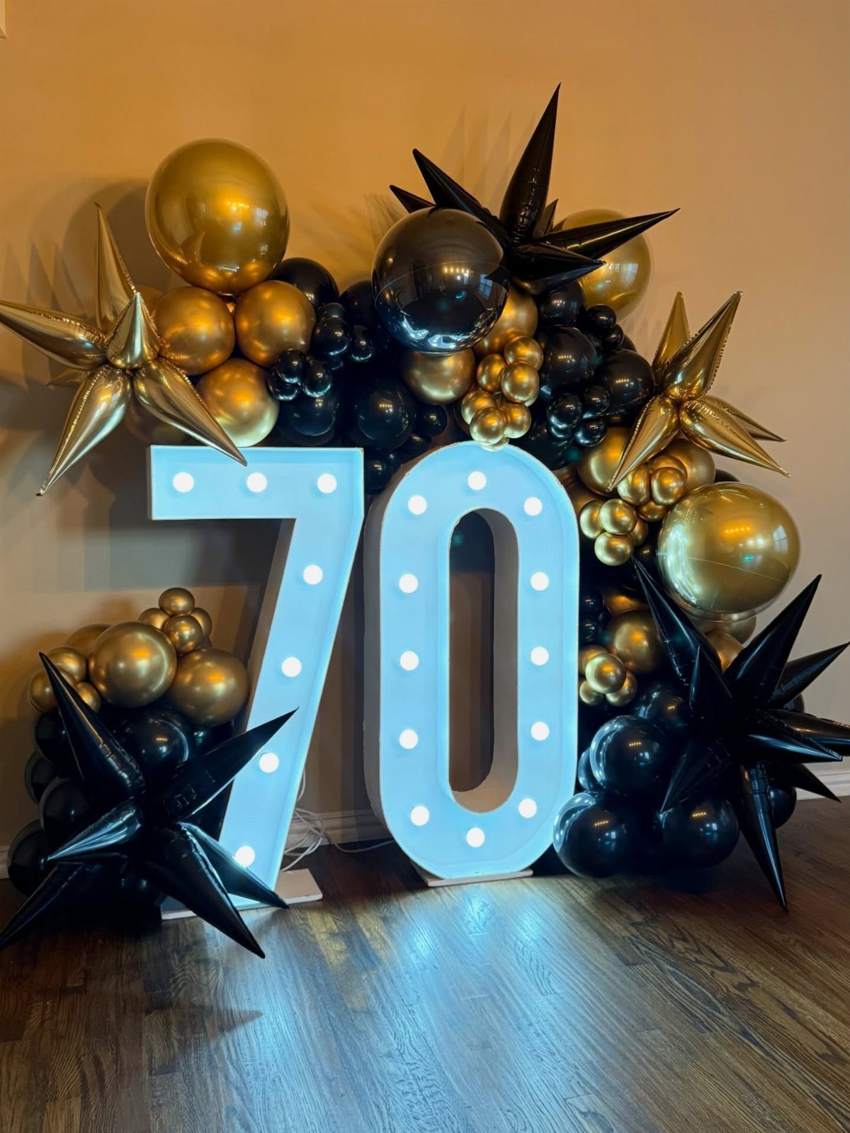 Illuminated number 70 surrounded by gold and black balloons for a birthday celebration.
