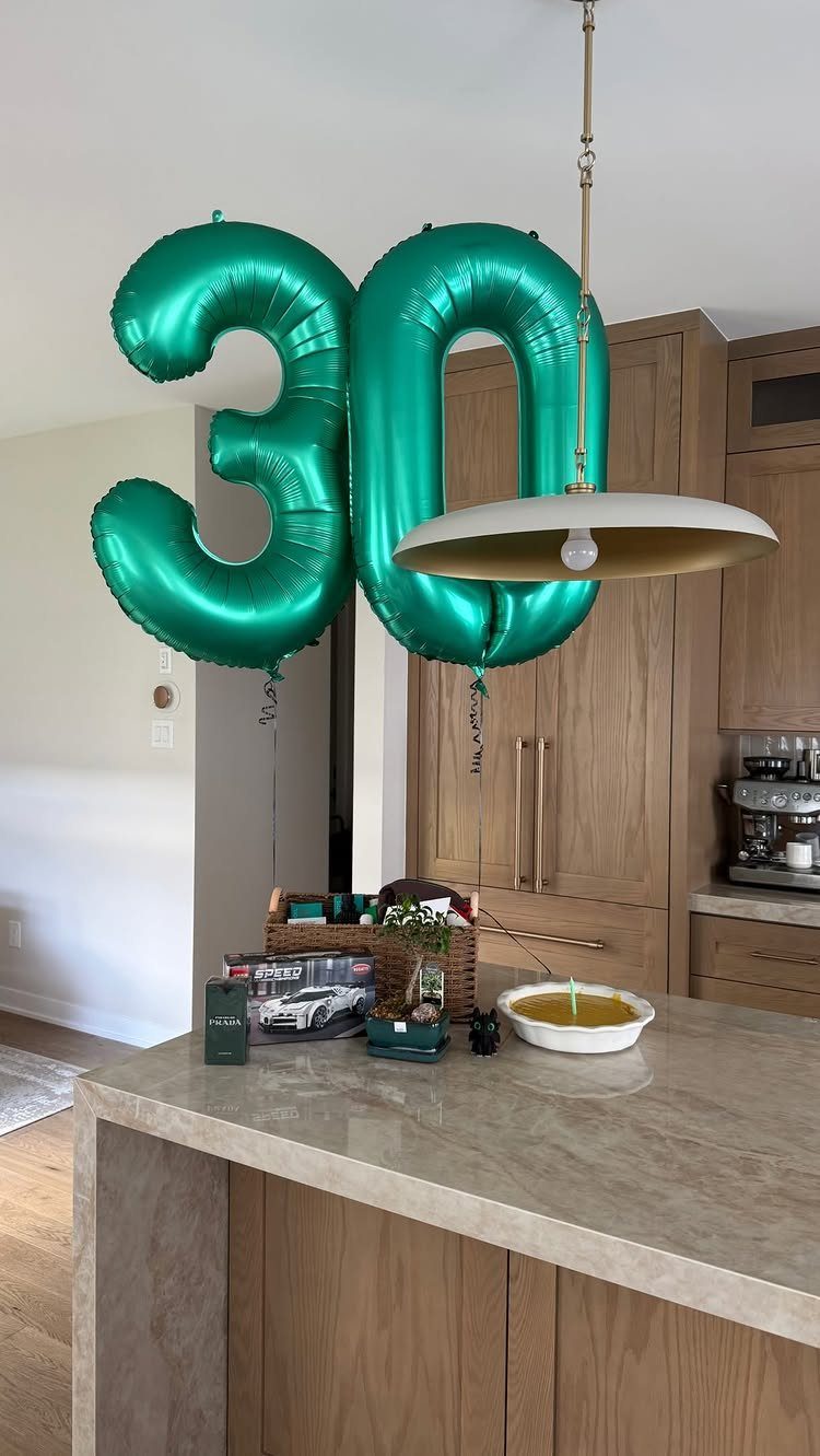 Green number 30 balloons floating above a birthday gift basket on a kitchen counter