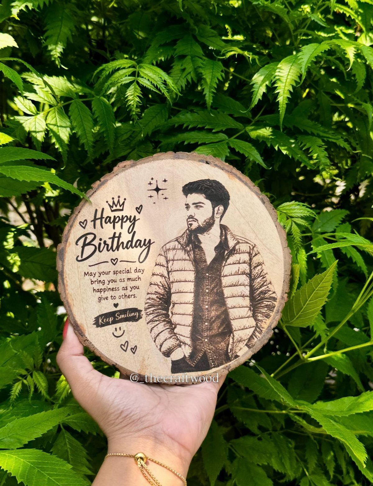 Engraved wooden slice with a man's portrait and birthday message held against greenery