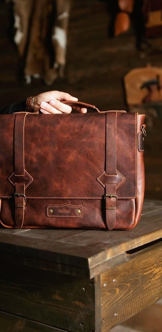 Brown leather briefcase with buckles resting on a rustic wooden table.