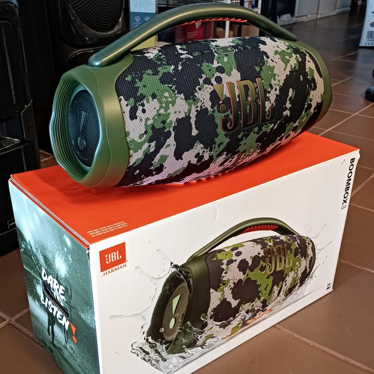 Camouflage JBL Boombox speaker resting on its orange and white retail packaging box.