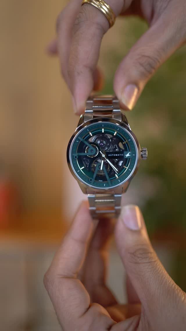 Silver automatic wristwatch with a green face held by two hands.