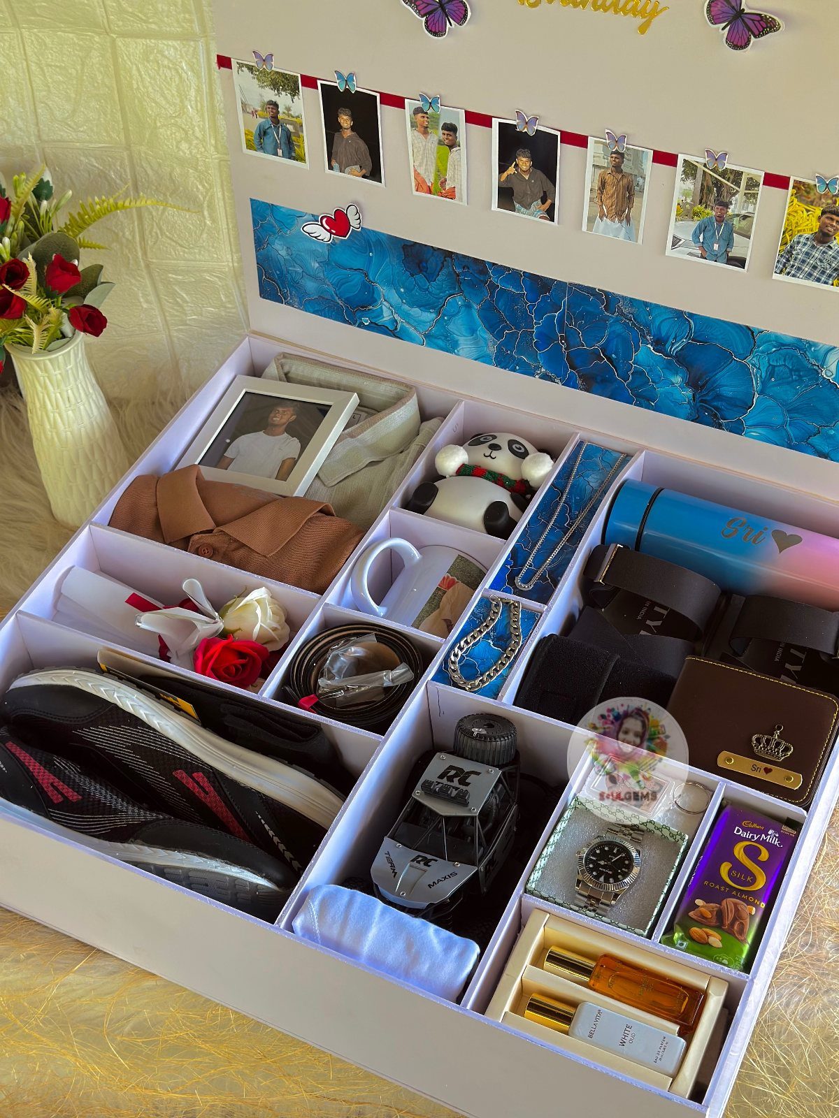 White gift box filled with sneakers, watch, perfume, and personal photos for a man.