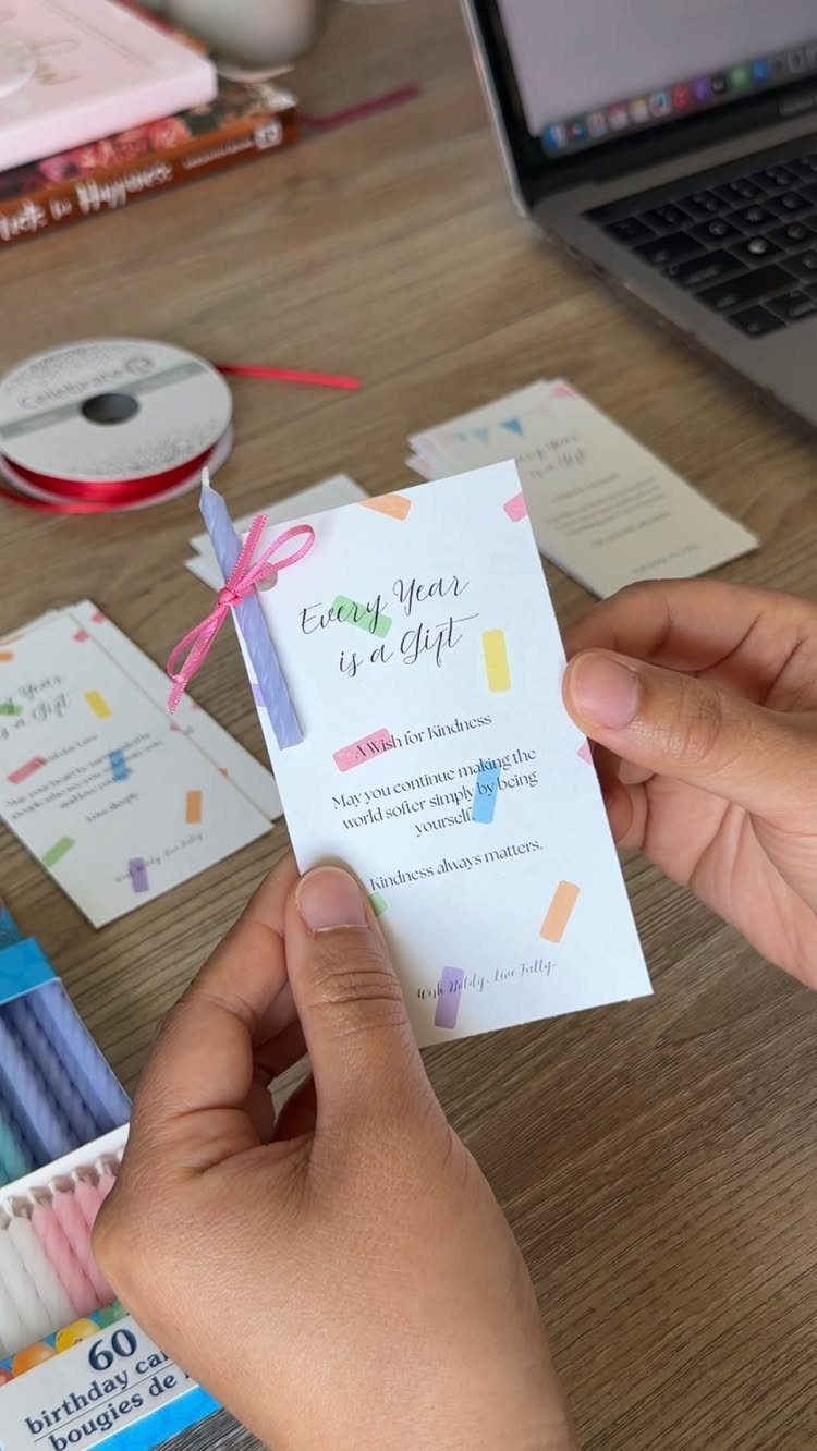 Hands holding a birthday card with a small purple candle tied with ribbon.