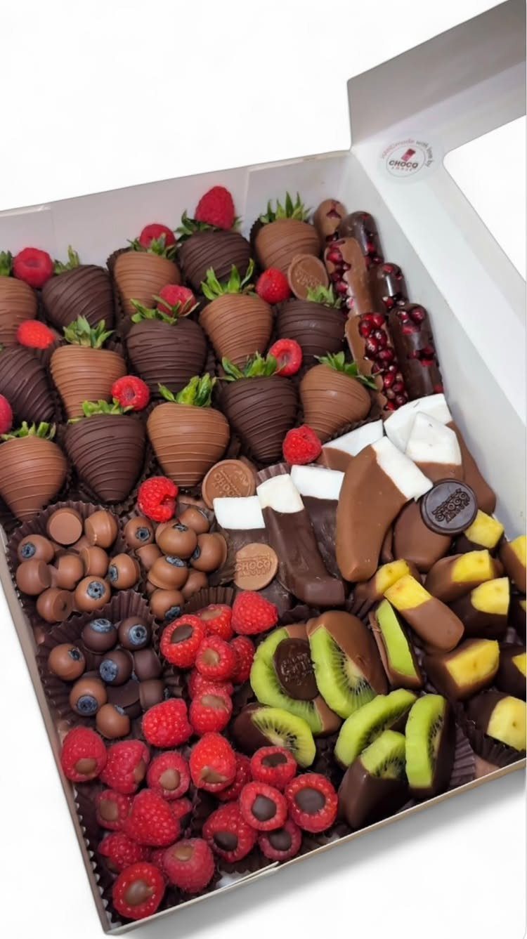 Chocolate-covered strawberries, kiwi, and bananas with fresh berries in a white gift box.