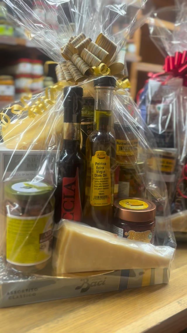 Gourmet gift basket with cheese, olive oil, and preserves wrapped in clear cellophane.
