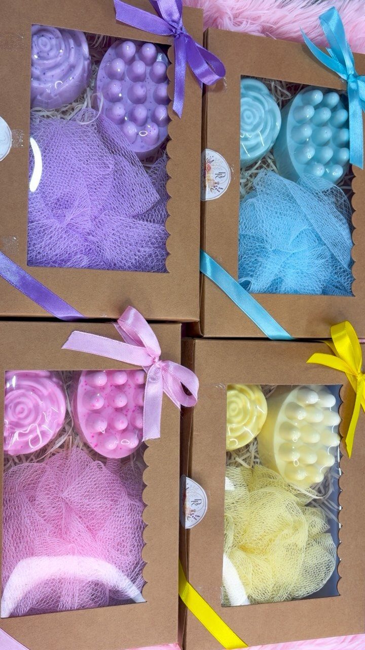 Four colorful bath gift sets in brown boxes with ribbons and loofahs.