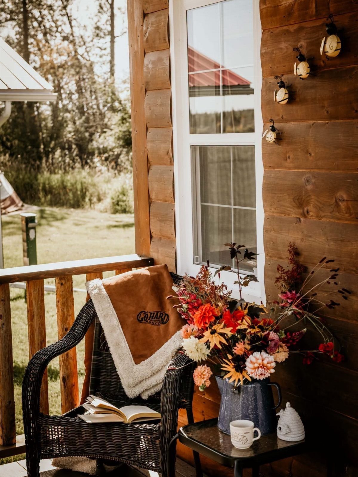 Wooden cabin porch with a wicker chair, autumn flowers, and an open book.