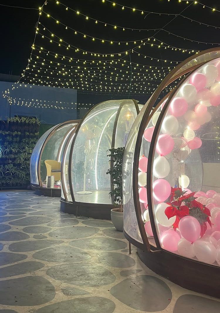 Clear plastic dome pods with pink and white balloons under outdoor string lights.
