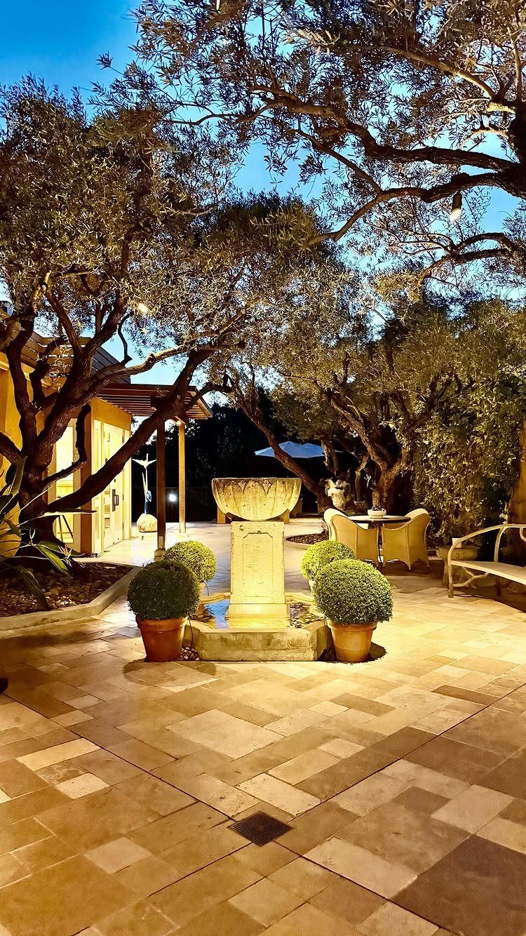 Stone patio with a central water fountain and large trees at dusk.