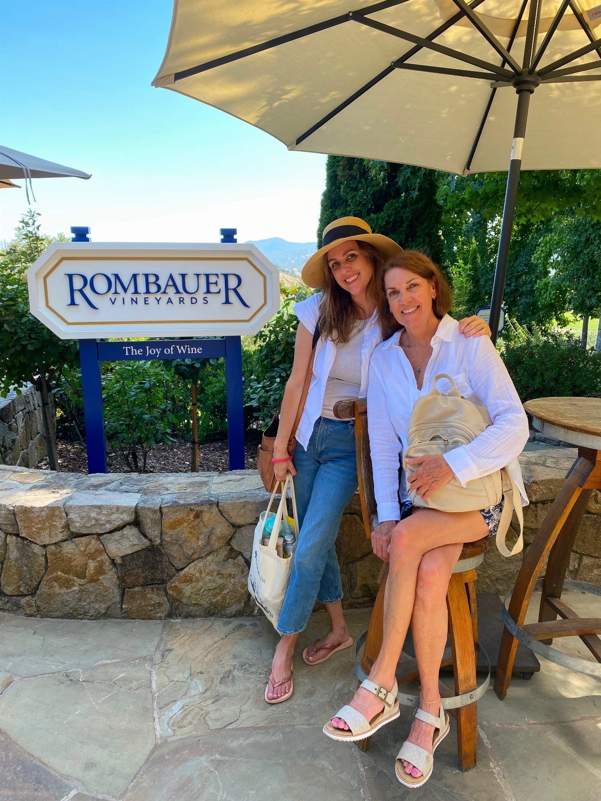 Two women posing in front of a Rombauer Vineyards sign at a winery.