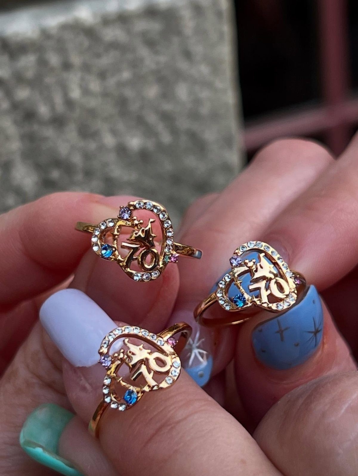 Gold heart rings with the number 70 and blue stones held by fingers.