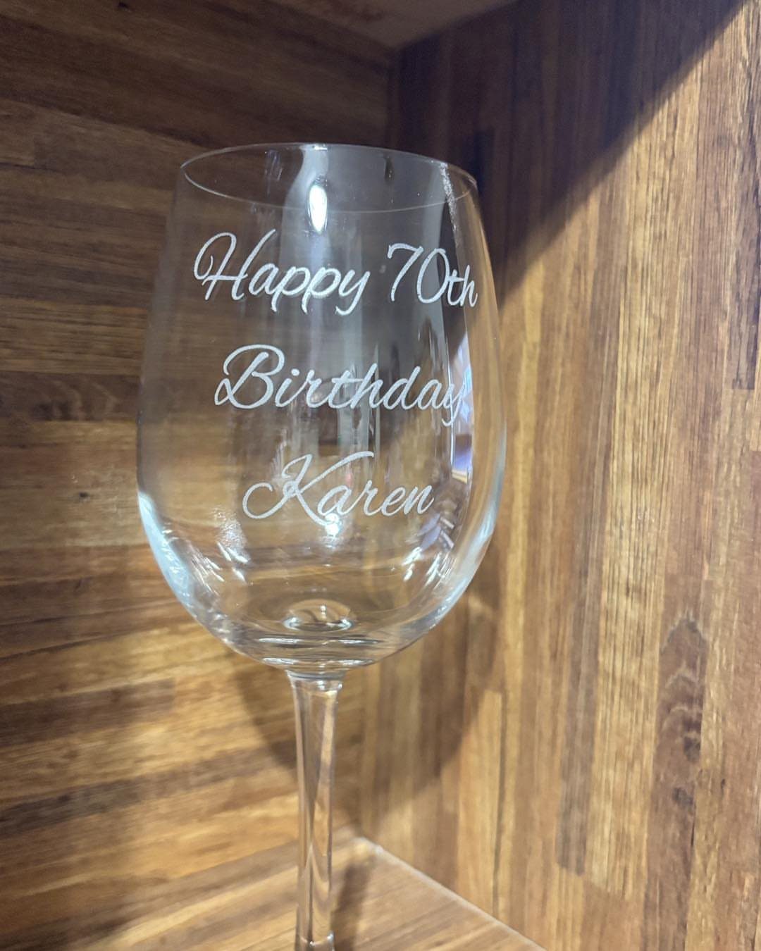 Engraved wine glass with Happy 70th Birthday Karen text against a wooden background