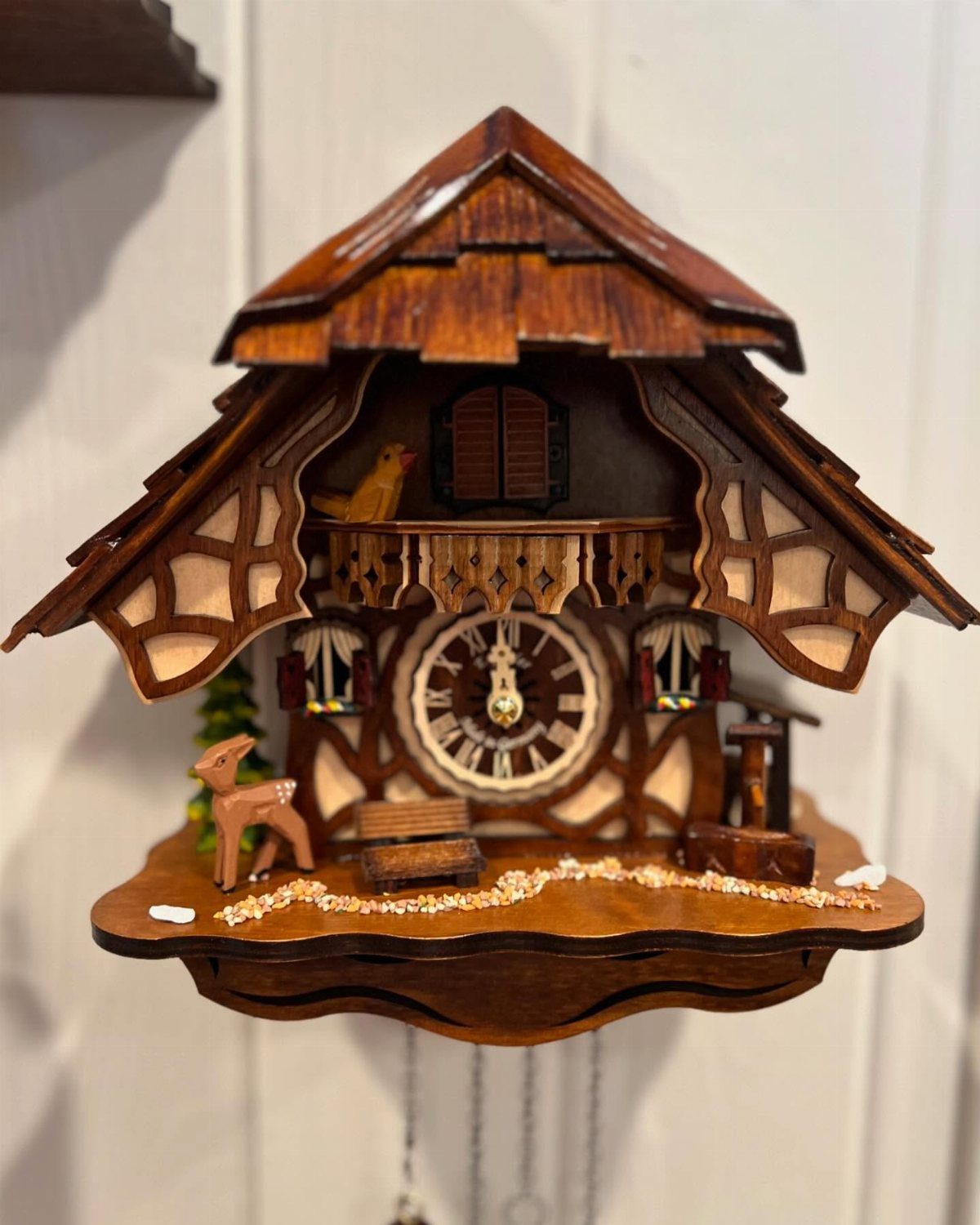 Ornate wooden cuckoo clock shaped like a chalet with a small deer figurine.