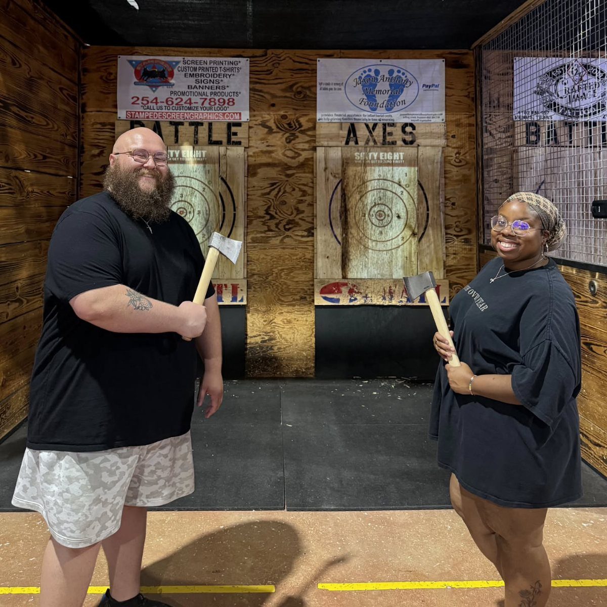 Man and woman holding axes in front of wooden targets at an axe throwing venue