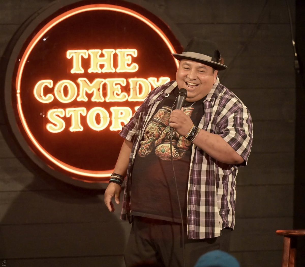 Comedian holding a microphone on stage in front of The Comedy Store sign